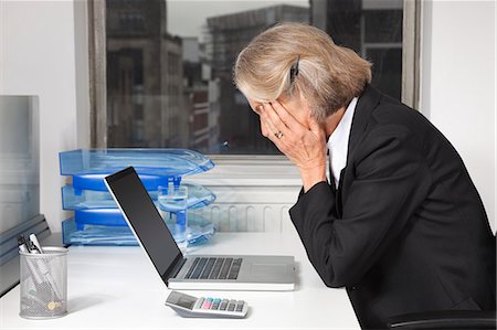 sitting at desk sideview - Side view of tired senior businesswoman in front of laptop at desk in office Stock Photo - Premium Royalty-Free, Code: 693-06497627