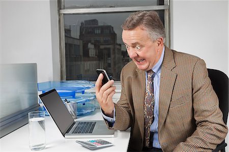 simsearch:400-04186486,k - Angry middle-aged businessman looking at cell phone in office Stock Photo - Premium Royalty-Free, Code: 693-06497635