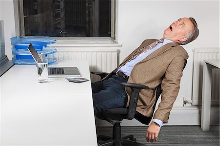 stressed - Side view of exhausted middle-aged businessman in front of laptop in office Stock Photo - Premium Royalty-Free, Code: 693-06497632