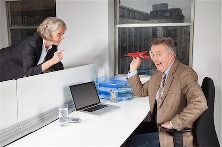 senior businessman in chair - Middle-aged businessman throwing paper airplane towards female colleague in office Stock Photo - Premium Royalty-Free, Code: 693-06497640