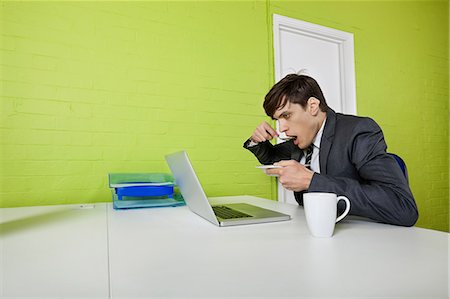 desk with wall - Side view of young businessman eating while using laptop at table Stock Photo - Premium Royalty-Free, Code: 693-06667975
