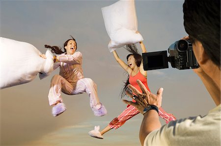 Man video recording two playful women in sleepwear having a pillow fight Stock Photo - Premium Royalty-Free, Code: 693-06667984