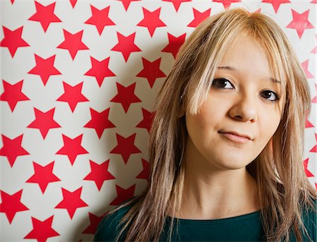 Close-up of beautiful young woman against red star shapes wallpaper Foto de stock - Sin royalties Premium, Código: 693-06667980