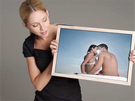 simsearch:693-06668015,k - Young businesswoman looking at photograph of couple at beach against gray background Photographie de stock - Premium Libres de Droits, Code: 693-06668017
