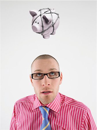 debt - Young businessman looking up at piggy bank tied with rope representing trapped finances Stock Photo - Premium Royalty-Free, Code: 693-06668010