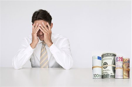 Worried businessman at table with money rolls representing financial problems Stock Photo - Premium Royalty-Free, Code: 693-06668013