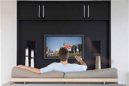simsearch:649-06533053,k - Back view of mid-adult man changing channels with television remote control in living room Foto de stock - Royalty Free Premium, Número: 693-06668024
