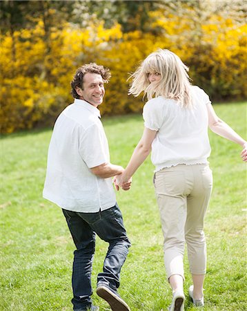 people running grass park - Couple holding hands with back to camera running through park Stock Photo - Premium Royalty-Free, Code: 693-06967439