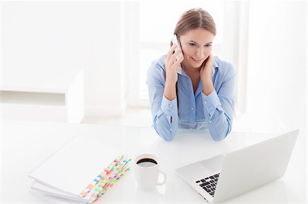 pictures of people seating on a table - Woman using cell phone and looking at computer Stock Photo - Premium Royalty-Free, Code: 693-07444413