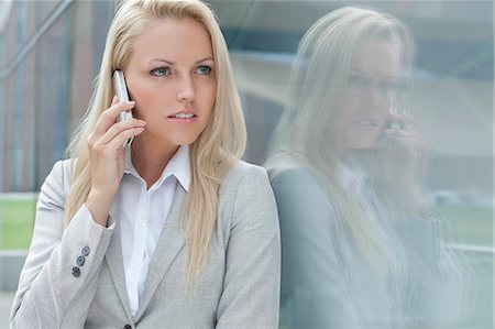 Beautiful young businesswoman conversing on cell phone while looking away by glass wall Stock Photo - Premium Royalty-Free, Code: 693-07444446