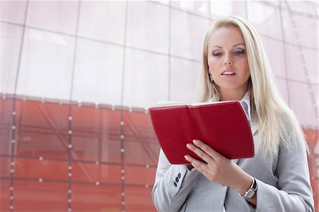 person reading note - Beautiful young businesswoman reading notes in organizer while standing against office building Stock Photo - Premium Royalty-Free, Code: 693-07444442