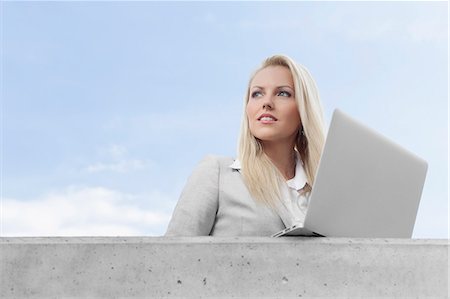 simsearch:693-07444453,k - Young businesswoman with laptop looking away on terrace against sky Foto de stock - Sin royalties Premium, Código: 693-07444451