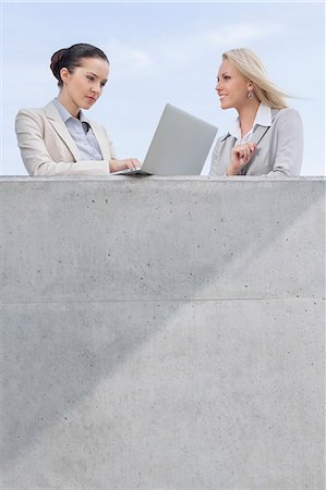 Low angle view of businesswoman using laptop while standing with coworker on terrace against sky Stock Photo - Premium Royalty-Free, Code: 693-07444453