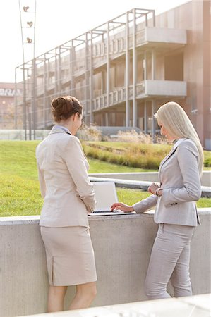 simsearch:693-07912336,k - Young businesswomen working together on laptop while standing against office building Foto de stock - Sin royalties Premium, Código: 693-07444462