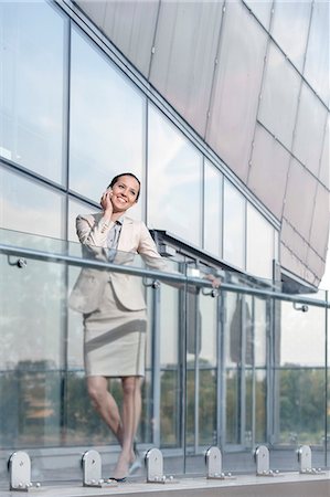 Full length of happy young businesswoman using cell phone at office balcony Stock Photo - Premium Royalty-Free, Code: 693-07444474