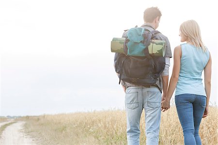 Rear view of young hiking couple holding hands while walking in countryside Stock Photo - Premium Royalty-Free, Code: 693-07444506