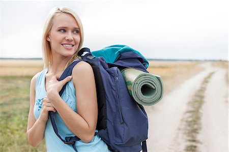 packing for travel - Beautiful woman with backpack looking away while hiking at field Stock Photo - Premium Royalty-Free, Code: 693-07444515