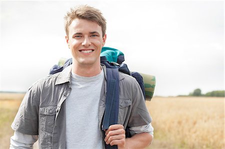 field alone smiling young man outdoors - Portrait of handsome male hiker with backpack standing on field Stock Photo - Premium Royalty-Free, Code: 693-07444513