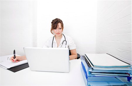 simsearch:400-03924532,k - Young female doctor with laptop writing notes on desk in clinic Stock Photo - Premium Royalty-Free, Code: 693-07444523
