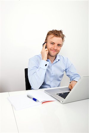 Portrait of confident businessman on call while using laptop in office Stock Photo - Premium Royalty-Free, Code: 693-07455858