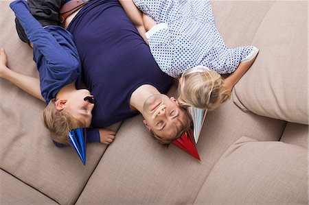 High angle view of father and children with artificial mustache and party hat sleeping on sofa bed Stock Photo - Premium Royalty-Free, Code: 693-07455881