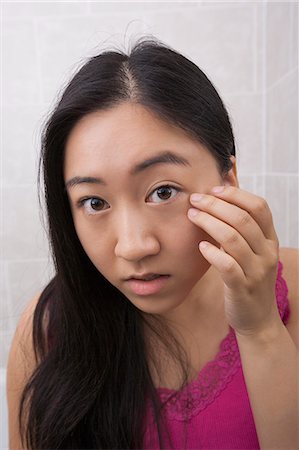 Portrait of beautiful young woman inspecting her face in bathroom Stock Photo - Premium Royalty-Free, Code: 693-07455937