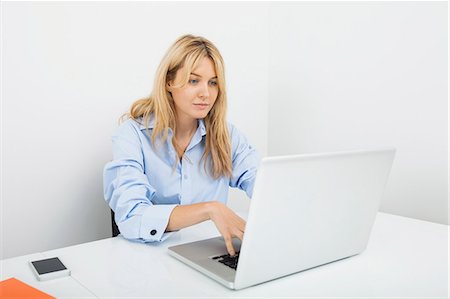 Young businesswoman using laptop at desk in office Foto de stock - Sin royalties Premium, Código: 693-07455976