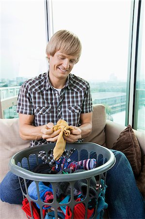 simsearch:693-07456039,k - Smiling mid-adult man with laundry basket sitting on sofa at home Foto de stock - Sin royalties Premium, Código: 693-07456007