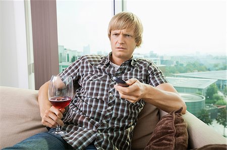 Displeased mid-adult man with wine glass watching television on sofa at home Stock Photo - Premium Royalty-Free, Code: 693-07456003