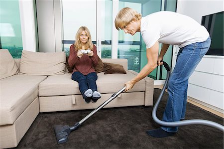 Man vacuuming while woman play video game in living room at home Stock Photo - Premium Royalty-Free, Code: 693-07456045