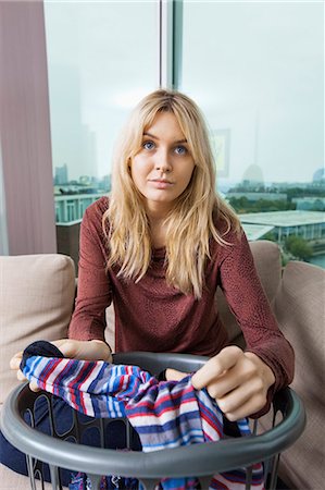 Portrait of young woman with laundry basket sitting on sofa at home Photographie de stock - Premium Libres de Droits, Code: 693-07456047