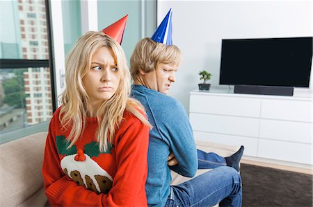 Annoyed couple in Christmas sweaters and party hats sitting back to back at home Foto de stock - Sin royalties Premium, Código: 693-07456041