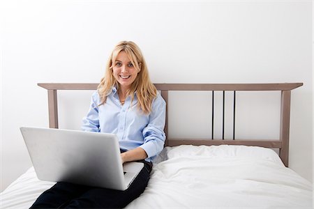 Portrait of happy businesswoman using laptop in bed Stock Photo - Premium Royalty-Free, Code: 693-07456089