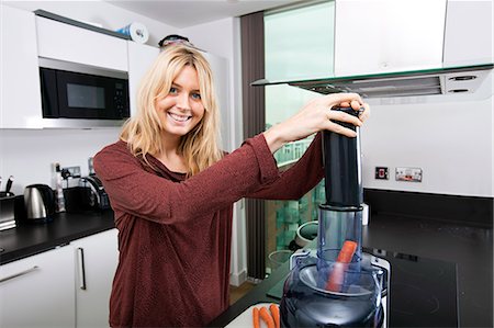 Portrait of young blond woman using juicer for juicing carrots in kitchen Foto de stock - Royalty Free Premium, Número: 693-07456080