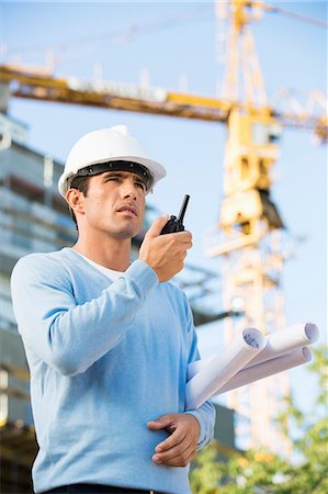 diseñador (hombre) - Male architect holding blueprints while using walkie-talkie at construction site Foto de stock - Sin royalties Premium, Código: 693-07456145