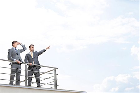 simsearch:693-07672655,k - Businessman showing something to coworker against cloudy sky Stock Photo - Premium Royalty-Free, Code: 693-07456193