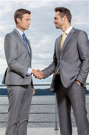 Businessmen shaking hands on terrace against sky Stock Photo - Premium Royalty-Free, Code: 693-07456200