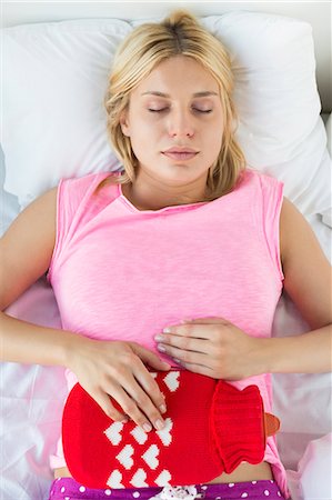 stomach pain - Young woman using hot water bottle on abdomen while lying on bed Stock Photo - Premium Royalty-Free, Code: 693-07456377