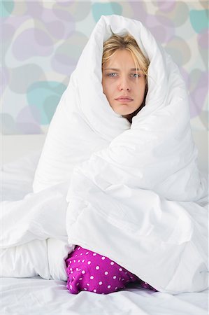 Portrait of young woman suffering from fever while wrapped in quilt in bed Stock Photo - Premium Royalty-Free, Code: 693-07456378