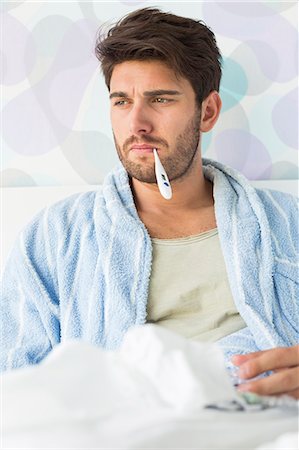 Sick man with thermometer in mouth sitting on bed Foto de stock - Sin royalties Premium, Código: 693-07456406