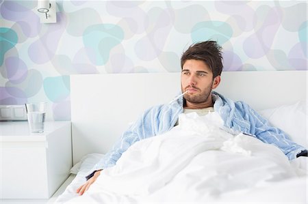 fever - Sick man with thermometer in mouth reclining on bed at home Stock Photo - Premium Royalty-Free, Code: 693-07456409