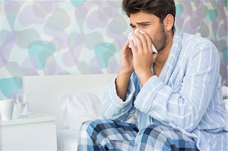 Sick man blowing his nose in tissue paper on bed at home Foto de stock - Sin royalties Premium, Código: 693-07456415