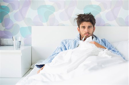 fiebre - Portrait of sick man with thermometer in mouth reclining on bed at home Foto de stock - Sin royalties Premium, Código: 693-07456410