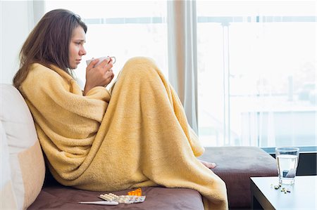 sick person - Side view of sick woman having coffee on sofa in living room Stock Photo - Premium Royalty-Free, Code: 693-07456420