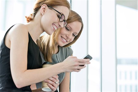showing - Smiling businesswomen using cell phone during break in office Stock Photo - Premium Royalty-Free, Code: 693-07542188