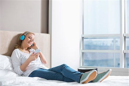 Full length of relaxed woman listening music in bedroom Foto de stock - Sin royalties Premium, Código: 693-07542208