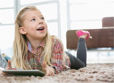 simsearch:6108-05867366,k - Cute girl with digital tablet looking away while lying on rug in living room Stock Photo - Premium Royalty-Free, Code: 693-07542216