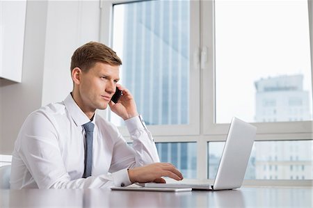 simsearch:693-07673302,k - Mid adult businessman on call while using laptop at home Stock Photo - Premium Royalty-Free, Code: 693-07542226
