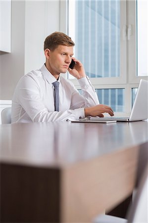 simsearch:693-07673302,k - Mid adult businessman on call while using laptop at home Stock Photo - Premium Royalty-Free, Code: 693-07542227