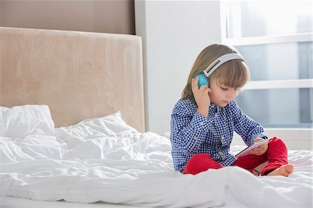 smartphone on bed - Full length of boy listening music on headphones in bedroom Stock Photo - Premium Royalty-Free, Code: 693-07542223